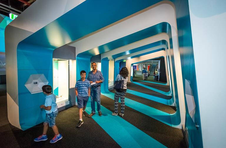 Four people walk through a blue and white tunnel in an exhibition space