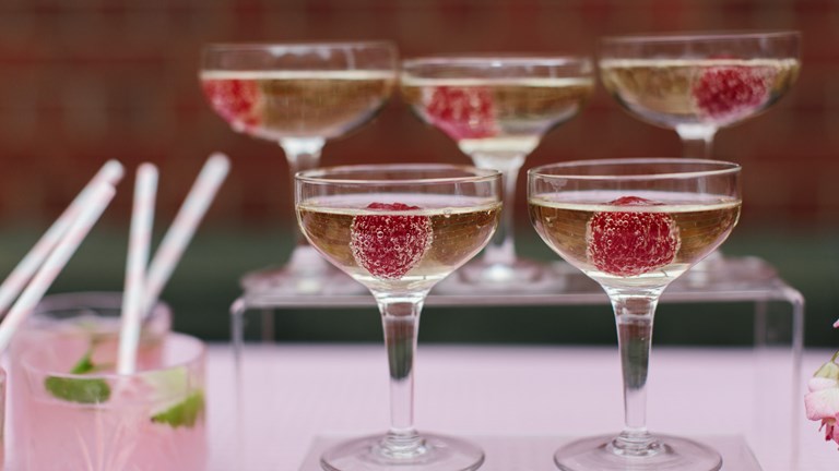 Five full champagne glasses with a raspberry in each 