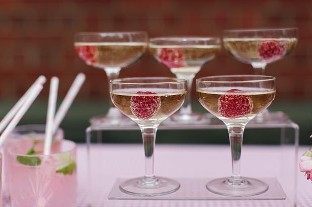 Five full champagne glasses with a raspberry in each 