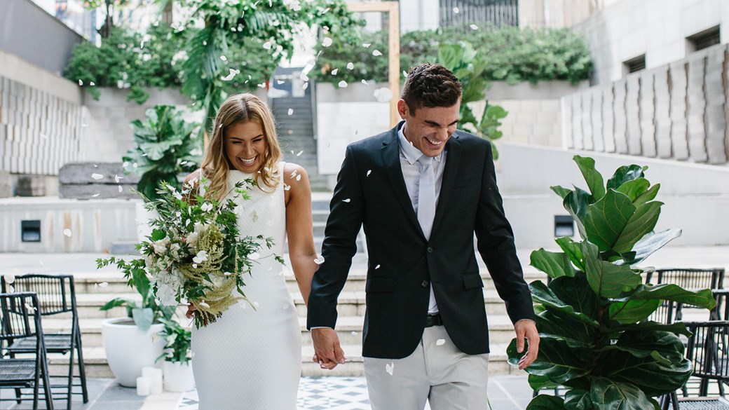 Bride and groom holding hands, looking down and smiling as they are being showered with confetti