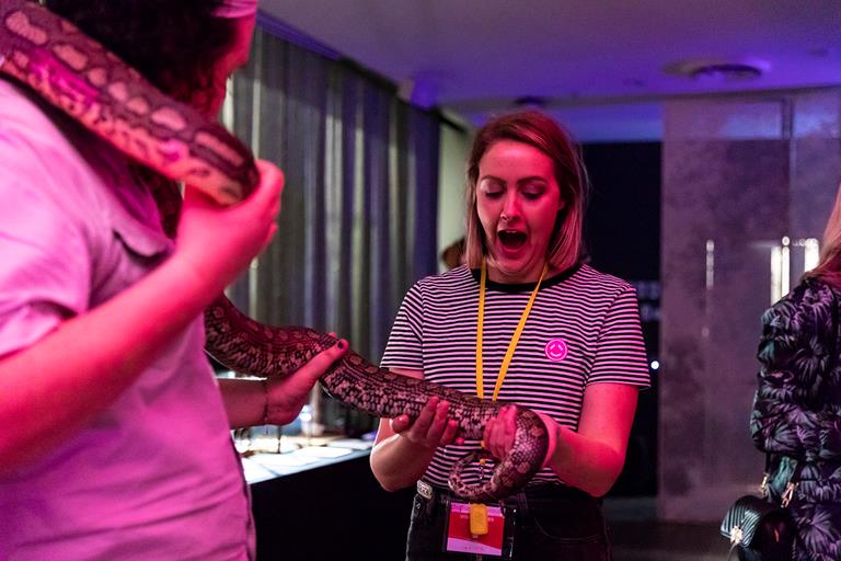 A woman with a look of exclamation on face as she meets a python being handle by a museum staff member