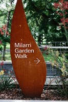 A sculpted wooden sign reading "Milarri Garden Walk" showing an arrow pointing to the right and with a park behind it