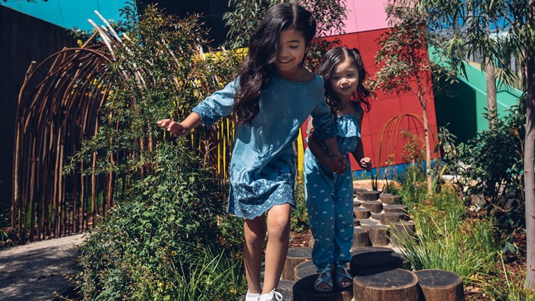 Two girls holding hands walking on stepping stones